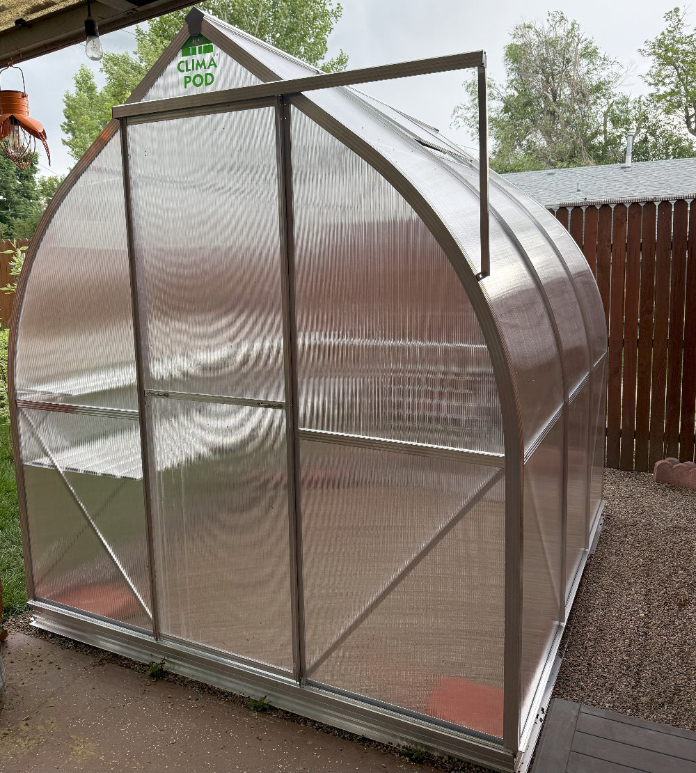 Small greenhouse with 'Clima Pod' branding in a backyard setting.
