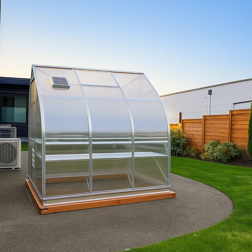 gotic arh polycarbonate greenhouse on a concrete patio with a wooden base, surrounded by grass and a fence.